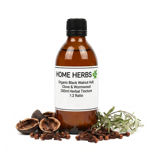An amber glass bottle of Home Herbs Organic Black Walnut Hull, Clove & Wormwood herbal tincture, surrounded by loose cloves, walnut halves, and a sprig of wormwood on a white background.