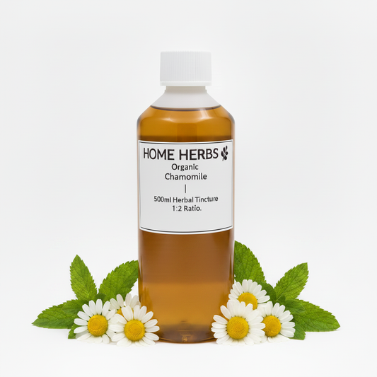 A 500ml bottle of Home Herbs Organic Chamomile herbal tincture, filled with amber liquid and topped with a white cap, displayed on a white background with chamomile flowers and green leaves at its base.