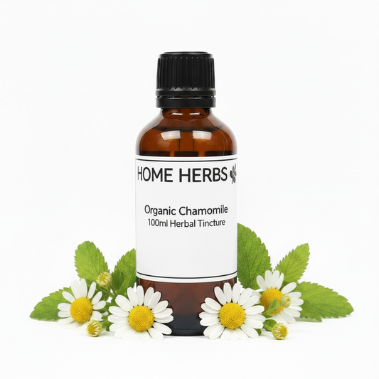 An amber glass bottle of Home Herbs Organic Chamomile 100ml Herbal Tincture, surrounded by fresh chamomile flowers and green leaves on a white background.