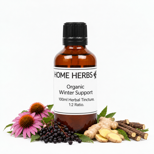 An amber glass bottle of Home Herbs Organic Winter Support herbal tincture, surrounded by its natural ingredients including echinacea purpurea, black elderberries, ginger root, and licorice root on a white background.
