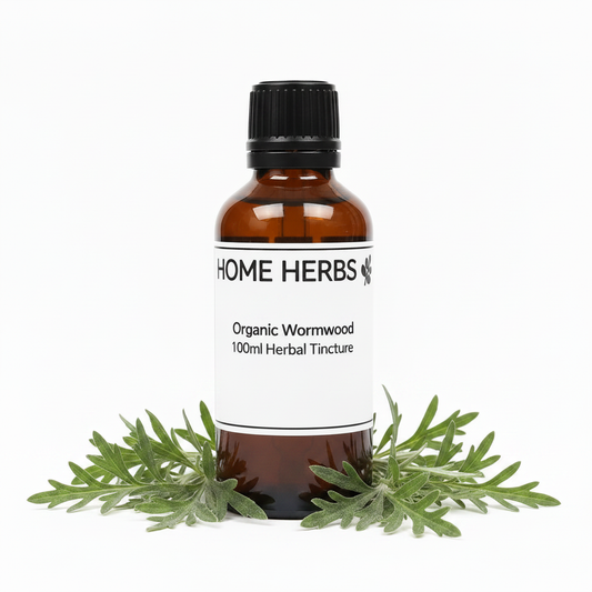 An amber glass bottle of Home Herbs Organic Wormwood 100ml Herbal Tincture with a white label and black cap, styled with fresh green wormwood leaves at the base on a white background.